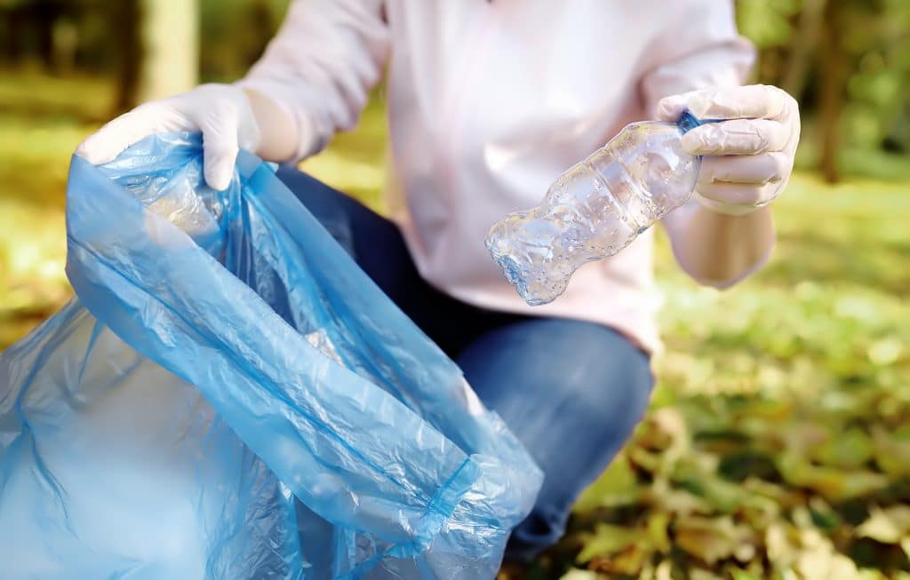 Volunteer picking up the garbage and putting it in biodegradable trash-bag on outdoors.